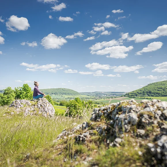 Blick vom Bubenheimer Berg Frau sitzt auf einem Stein in Yogapose im Vordergrund ein Felsen