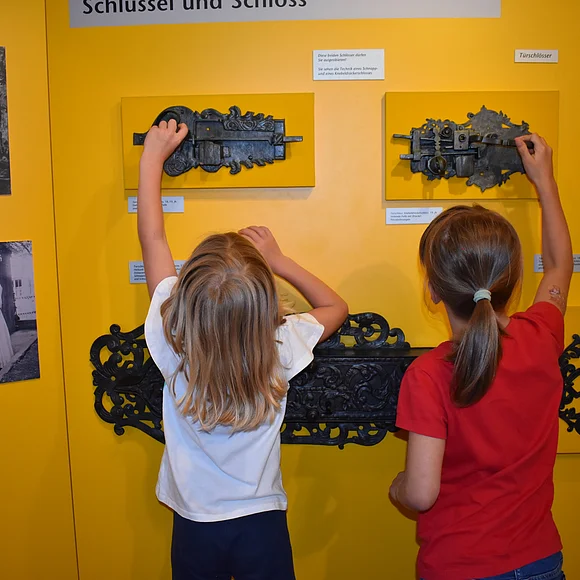 Zwei Kinder probieren alte, an der Wand befestigte Schlösser aus