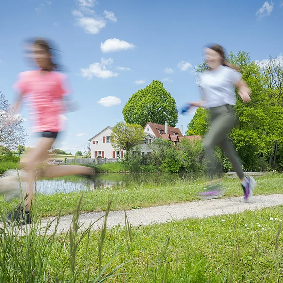 Zwei Mädchen rennen auf dem Weg neben dem Karlsgraben hintereinander. Die Mädchen sind leicht verschwommen.