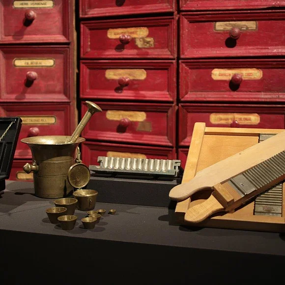 Blick auf einen alten Apothekerschrank. Im Vordergrund stehen ein Mörser und andere Apothekerutensilien