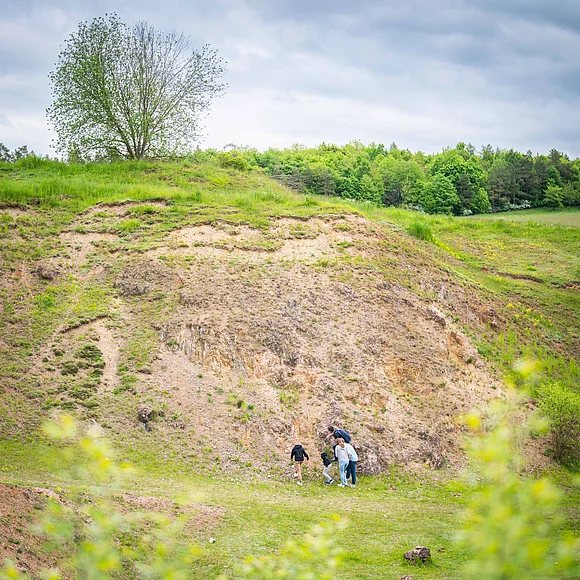 Eine Gruppe von Personen steht am Fuß eines Hanges mit spärlicher Vegetation und Spuren von Auswaschung.