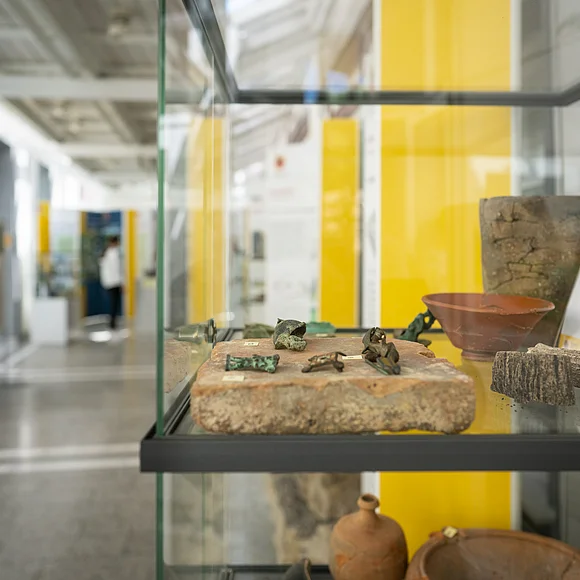 In einer Glasvitrine liegen verschiedene kleine archäologische Fundstücke.