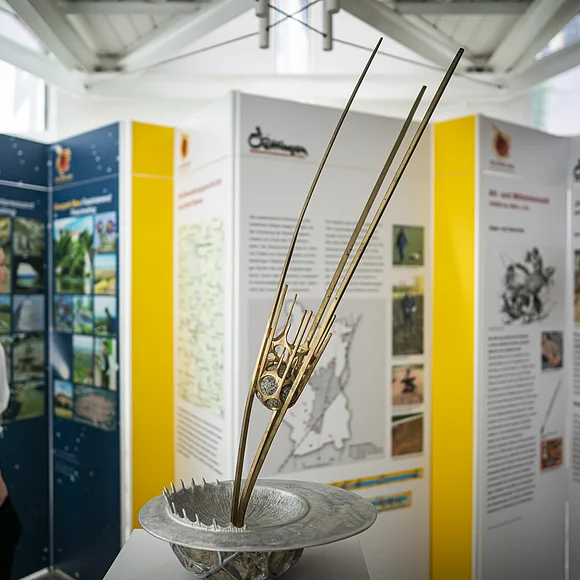 Eine Skulptur zeigt einen Asteroiden vor dem Einschlag in die Erdoberfläche. Im Hintergrund betrachtet ein Mädchen verschiedene Informationstafeln.