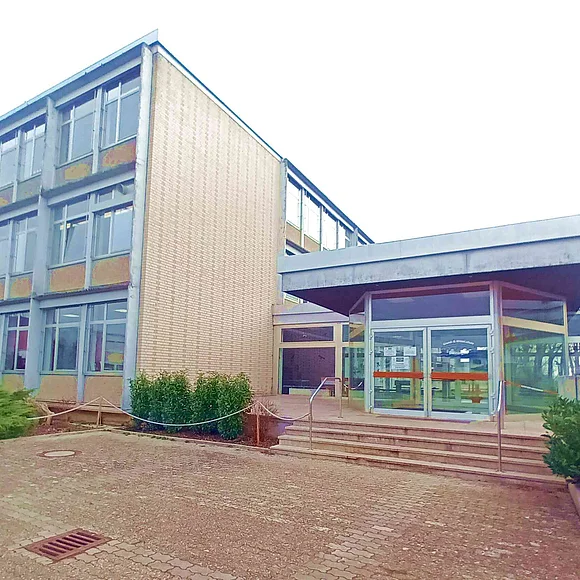 Ein dreistöckiges Gebäude hat eine Seitenwand aus Ziegeln und einen verglasten Eingangsbereich.