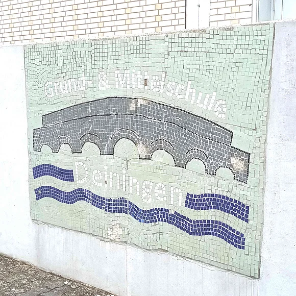 Ein Mosaik an einer Hauswand zeigt eine steinerne Brücke und den Schriftzug "Grund- & Mittelschule Deiningen".