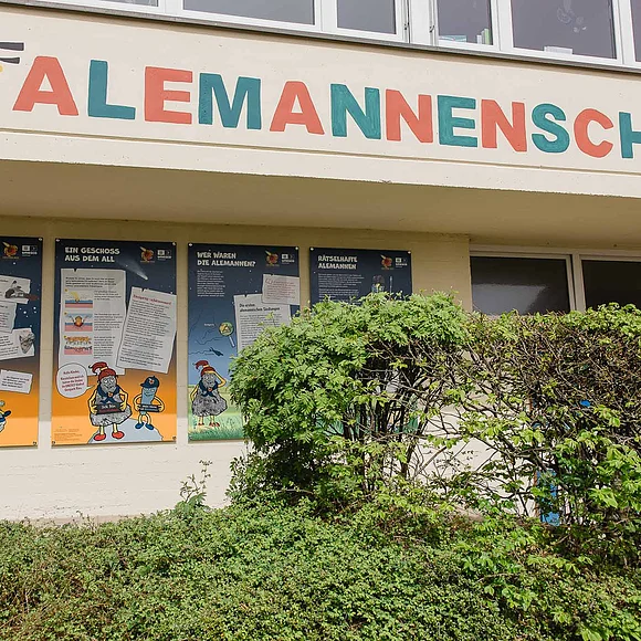 An einer Hauswand sind vier Informationstafeln für Kinder angebracht. Darüber steht in Großbuchstaben "Alemannenschule".