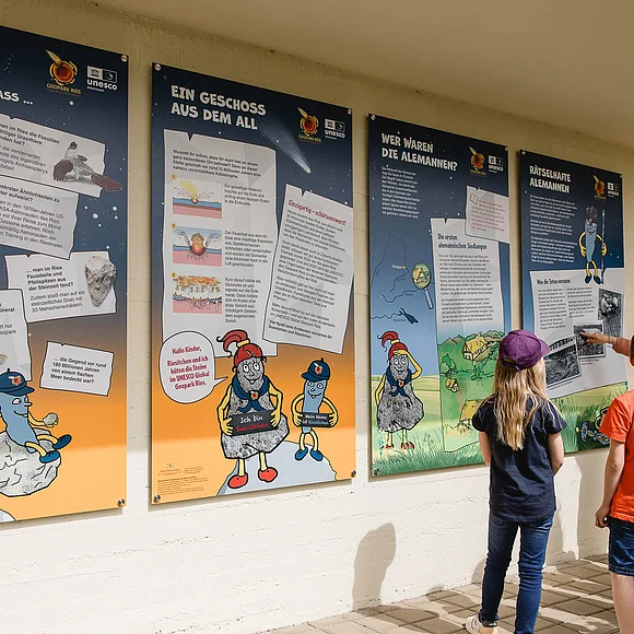 Eine Gruppe Kinder steht vor Informationstafeln, die an einer Hauswand angebracht sind.