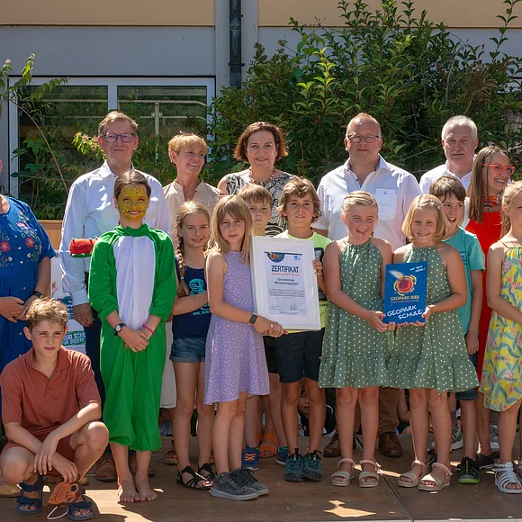 Gruppenbild mit Erwachsenen und Kindern, die das Zertifikat und das Schild "Geopark Ries Schule" in Händen halten.