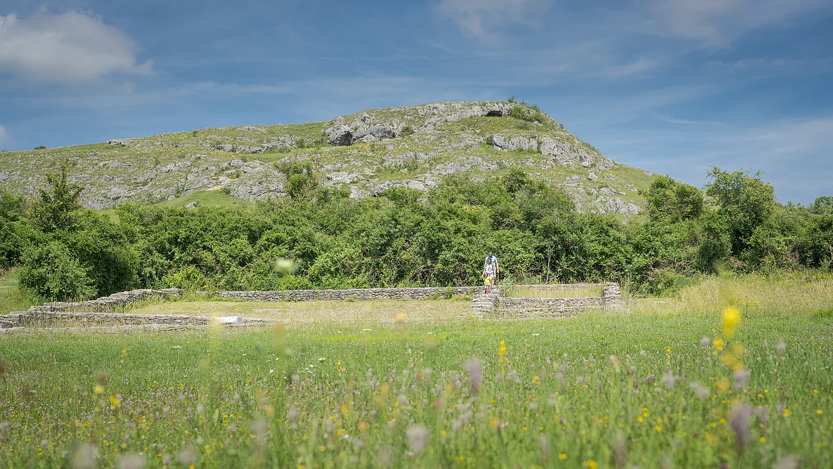 Geopark-Shooting 2021 Auf einer Wiese finden sich Grundmauern eines Gebäudes. Dahinter erhebt sich ein felsiger Hügel.
