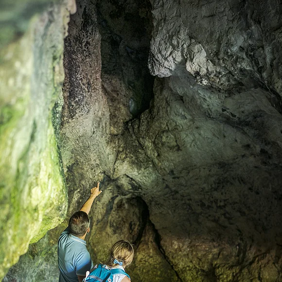 Eine Familie steht in einer Höhle. Der Mann deutet mit dem Finger an die Höhlendecke.