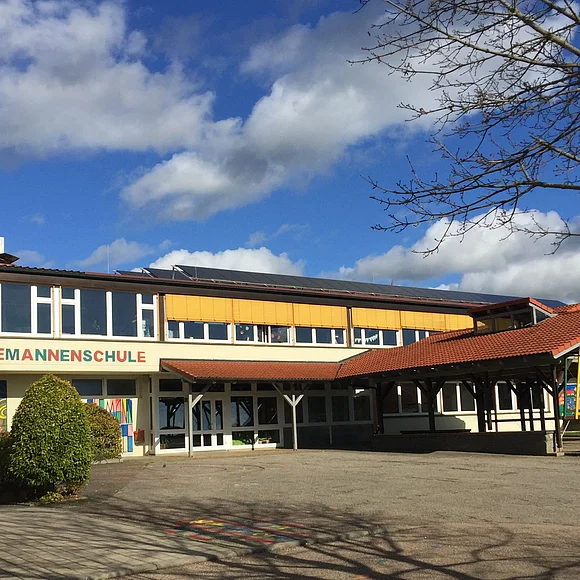 Ein zweistöckiges Gebäude mit einem großen überdachten Eingangsbereich trägt die Aufschrift "Alemannenschule".