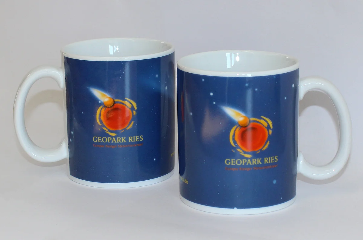 Zwei weiße Porzellantassen zeigen jeweils das Logo des Geopark Ries auf dunkelblauem Hintergrund.
