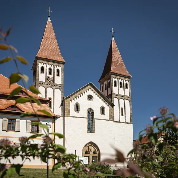 Das Kloster mit seinen zwei Türmen inmitten grüner Büsche. Der Himmel strahlt wolkenlos.