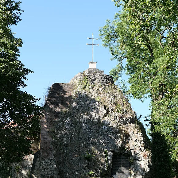 Ein hoher Felsblock trägt ein Kreuz obenauf und eine Inschrifttafel.