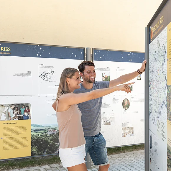Ein Mann und eine Frau betrachten eine Informationstafel über den Geopark Ries.