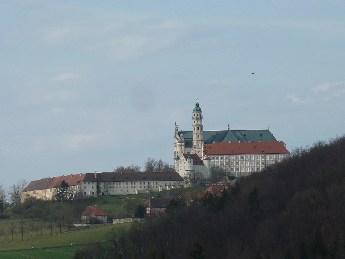 Auf einer Anhöhe befinden sich mehrere langgestreckte Gebäude, an die sich eine Kirche anschließt.