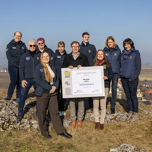 Gruppenfoto des Teams des Geopark Ries mit der Urkunde der International Union of Geological Sciences. Im Hintergrund erstreckt sich in einer Senke eine weite Landschaft.