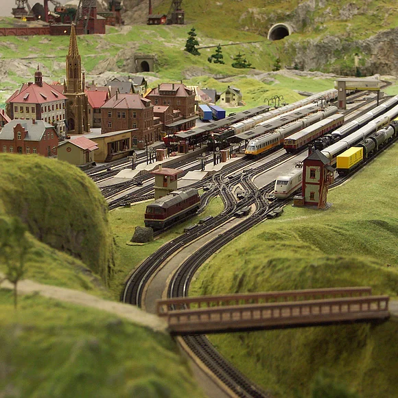 Eine Miniaturlandschaft umgeben von grün. Eisenbahnschienen und ein Dorf.