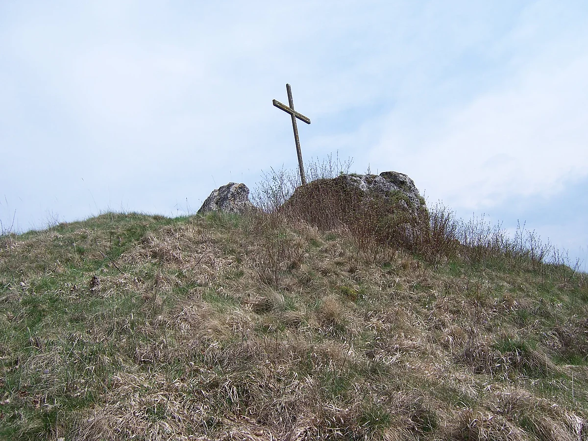 Auf der Kuppe eines Hügels befinden sich zwei Felsbrocken und ein kleines Holzkreuz.
