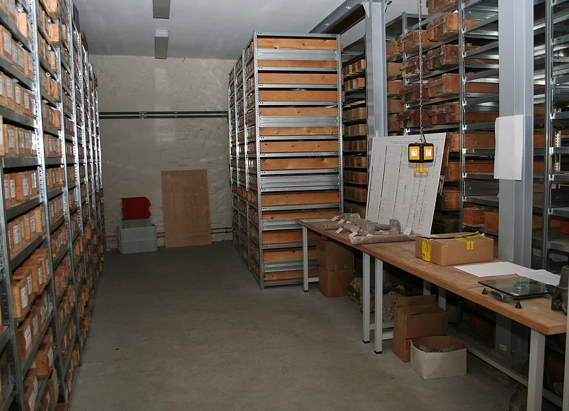 In einem Raum stehen mehrere Metallregale mit Holzkästen, die beschriftete Bohrkerne enthalten.