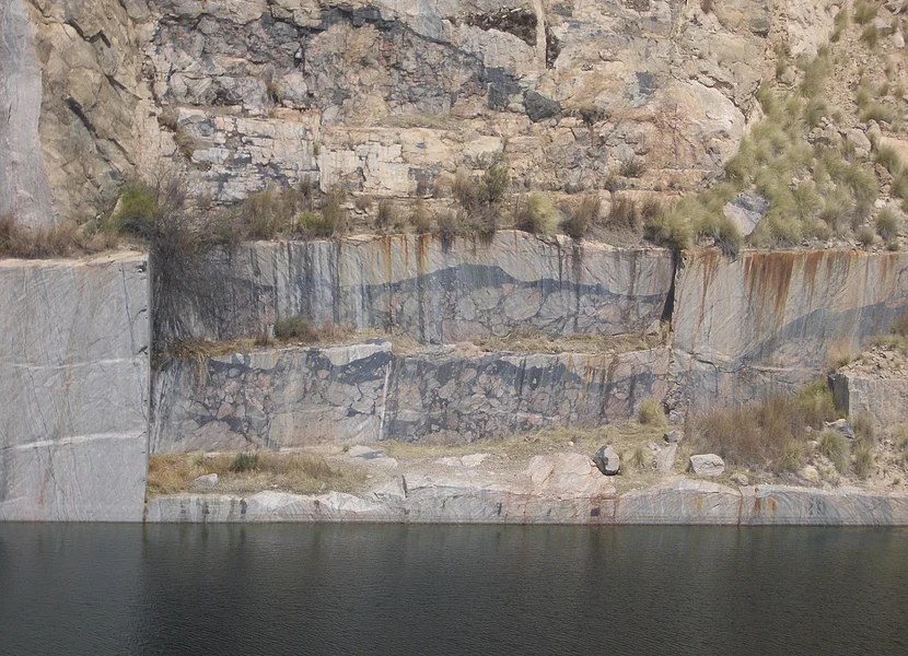 Unterhalb der stufigen Wand eines Steinbruchs befindet sich ein See.