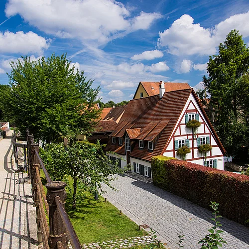 Der Weg auf einer Stadtmauer ist mit Geländern begrenzt. Neben der Mauer befindet sich ein gepflasterter Weg und ein Haus mit rotem Fachwerk.