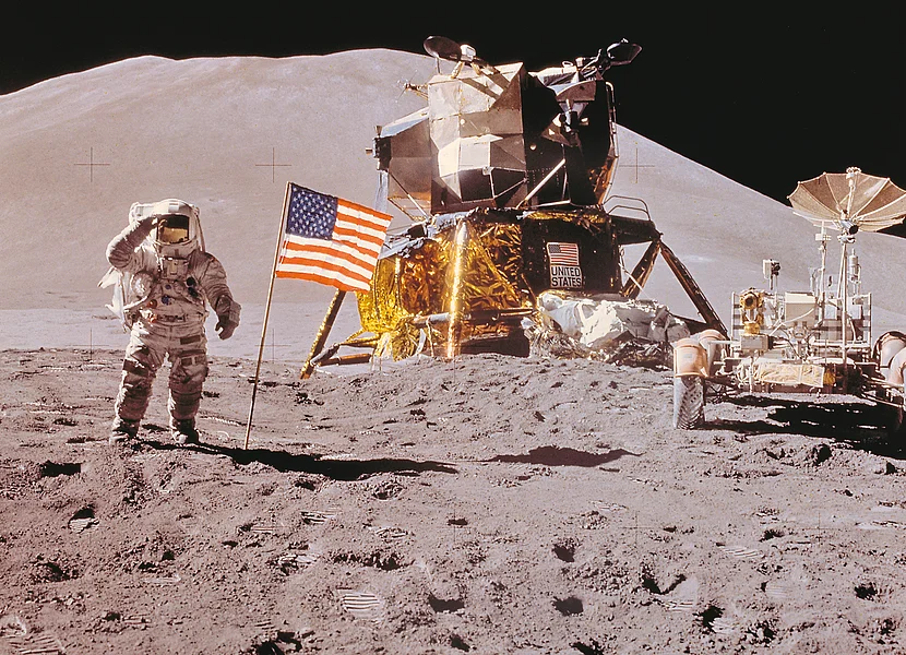 Ein Astronaut steht neben einer USA-Flagge auf der Mondoberfläche. Im Hintergrund sind zwei Mondrover zu sehen.