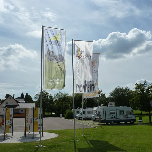 Die Geopark Infostelle mit Flaggen und im Hintergrund die Wohnmobile auf dem Wohnmobilstellplatz in Monheim.