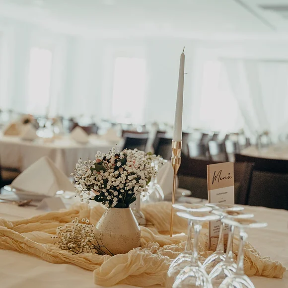Blick auf einen in hellen Farben gedeckten Tisch mit Gläsern, Blumenvase und Kerze.