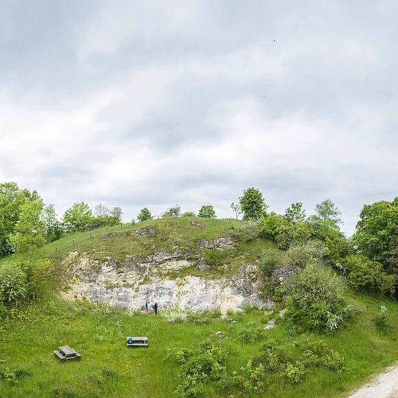 Geopark Ries Mai 2023 Vor einem geologischen Aufschluss stehen auf einer Wiese Sitzbänke und eine Informationstafel.