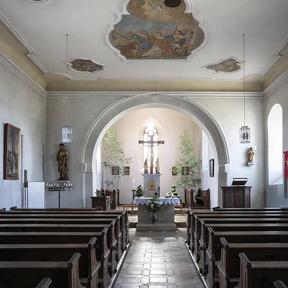 Innenraum einer Kirche mit Bänken, Altar und bemalter Decke.