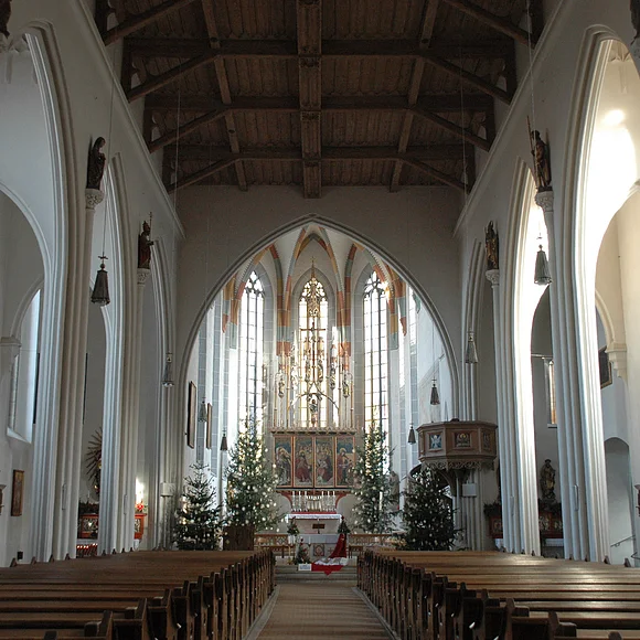 Blick in das lichtdurchflutete Innere mit dem Hauptaltar der von vier wegeschmückten Christbäumen umrahmt ist. Rechts vor dem Altar sieht man die Kanzel.