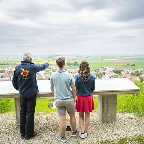 Ein Geopark Ries Führer zeigt einem Pärchen den Blick in den Rieskrater.