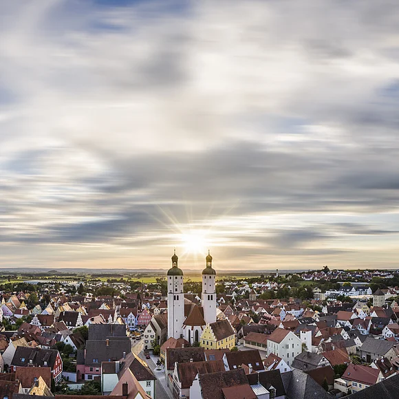 Panoramablick auf Stadt mit roten Dächern und zwei Kirchtürmen bei Sonnenuntergang unter bewölktem Himmel