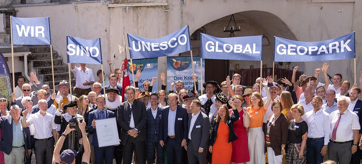 Eine große Gruppe Personen hält Banner mit der Aufschrift "Wir sind UNESCO Global Geopark" in die Höhe.