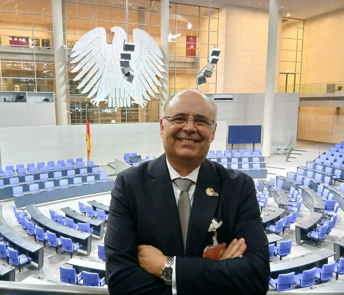 Artur Sá (Vorsitzender GGN) steht vor den Sitzreihen im Deutschen Bundestag. Im Hintergrund der Bundesadler.