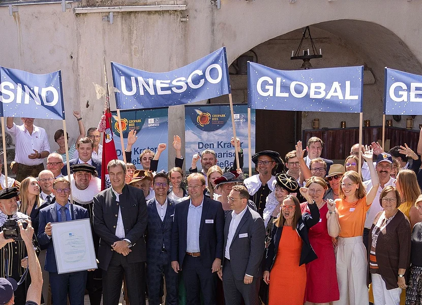 "Wir sind UNESCO Global Geopark" Eine große Gruppe Personen hält Banner mit der Aufschrift "Wir sind UNESCO Global Geopark" in die Höhe.