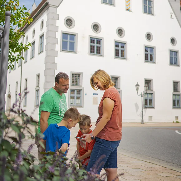 Eine Familie steht auf einer gepflasterten Straße vor einem historischen Gebäude mit Giebeldach.